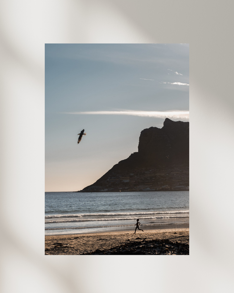 Young boy running alone along the beach at dusk in Houtbay Capetown — fine-art photograph by Kayleigh Groenendijk